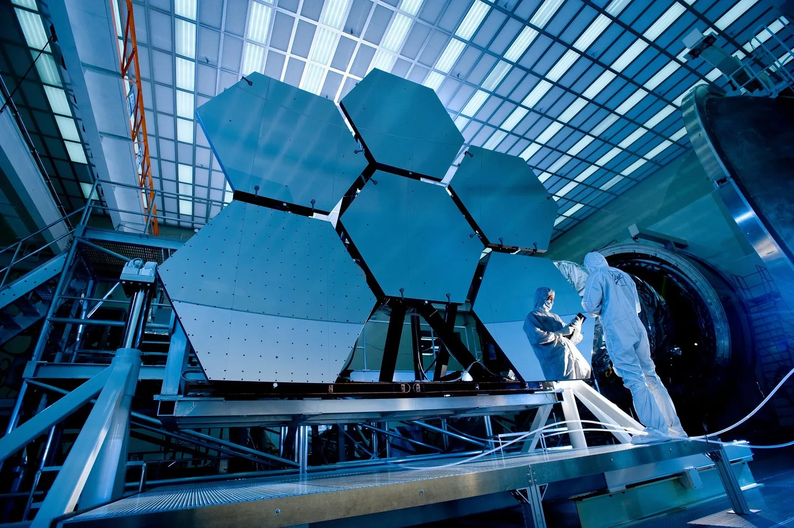 Technicians in clean-room suits inspecting large hexagonal telescope mirror segments