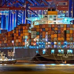 A container ship stacked with cargo at a brightly lit port terminal