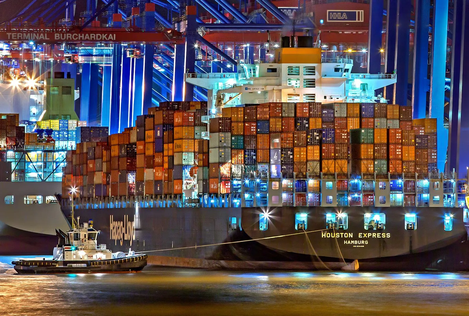 A container ship stacked with cargo at a brightly lit port terminal