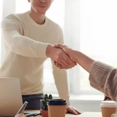 Two people shaking hands across a desk in a bright office