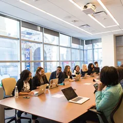 People seated around a long table in a bright meeting room with laptops open