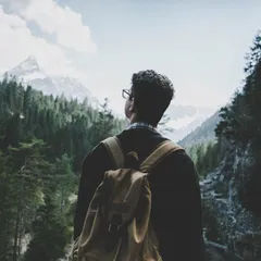 A hiker with a backpack looking out over a forested mountain valley